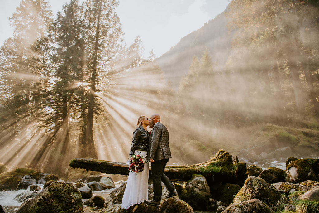 Couple sharing their first kiss under the misty sun rays at their waterfall elopement location during their BC elopement package