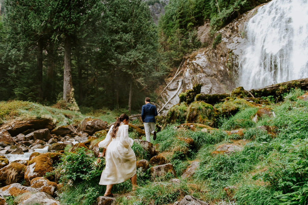 Couple walking underneath Chatterbox Falls in the Princess Louisa Marine Provincial Park during their British Columbia Elopement Package.