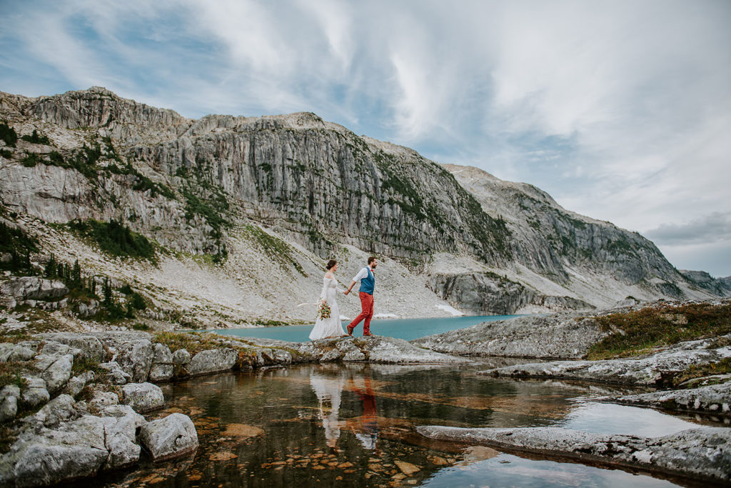 A couple walking along the shores of an Alpine lake during their elopement with B.C Elopement Photograher Paige Lorraine Photography